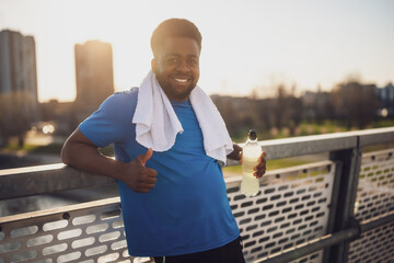 Portrait of young african-american man who is drinking water and relaxing after jogging. - 791406304