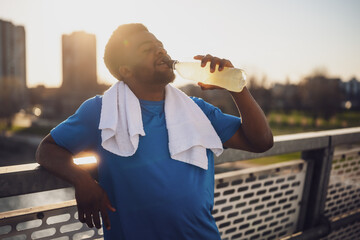 Portrait of young african-american man who is drinking water and relaxing after jogging. - 791406325