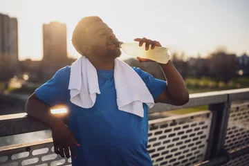 Fotobehang Portrait of young african-american man who is drinking water and relaxing after jogging. © djoronimo