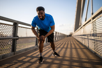 Young african-american man is injured while jogging. He has pain in knee. - 791406356