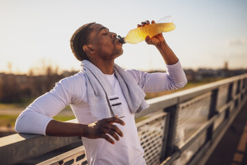 Portrait of young african-american man who is drinking water and relaxing after jogging. - 791406369