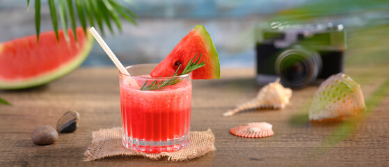Fresh watermelon juice, seashells and camera on wooden table. Summer vacation and travel concept