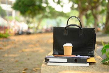 Closeup of briefcase, takeaway coffee cup and document on concrete bench. City life concept