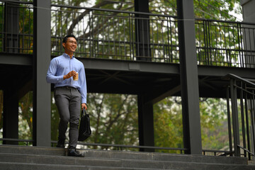 Confident smiling young businessman walking down the staircase outside his office