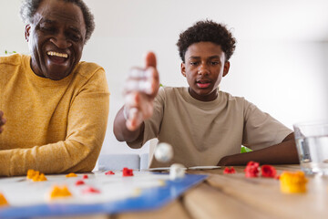 Happy senior man playing board game with grandson at home