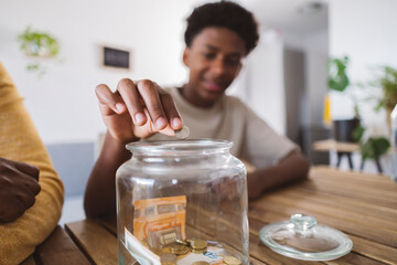 Teenage boy putting coin in savings jar by grandfather at home