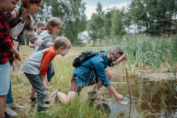Teacher showing lake water to school children, during field teaching class. Outdoor active education helping young student to learn about ecosystem.