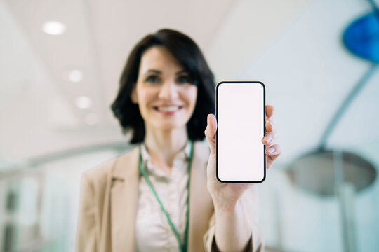 Smiling businesswoman showing smart phone with blank screen at office