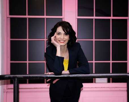 Smiling businesswoman leaning on railing near pink window