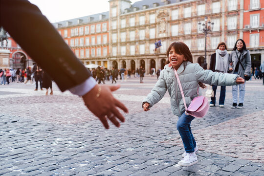 Cheerful girl running towards father at town square