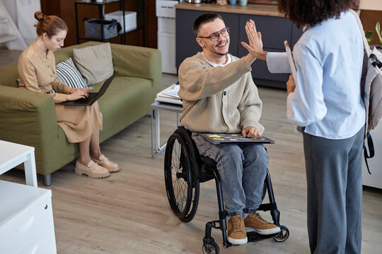 Businesswoman giving high-five to disabled colleague sitting in wheelchair at office