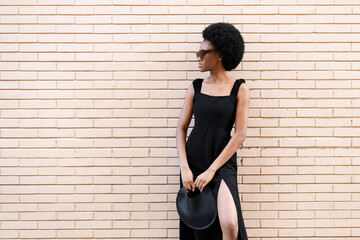 Fashionable Afro woman in black dress in front of brick wall