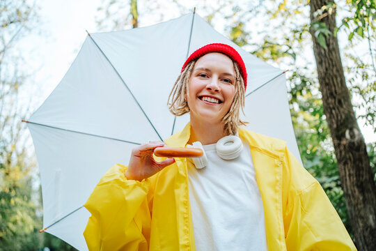 Happy young woman wearing yellow raincoat and holding white umbrella in park