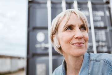 Blonde Woman in Denim Shirt Sitting Outdoors by Gray Container