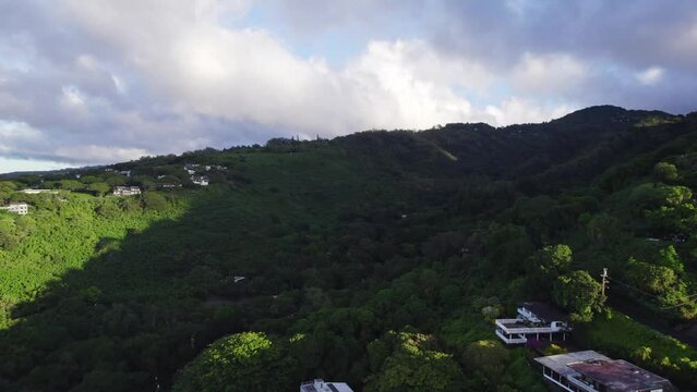 arial shot over a lush green  shaded mountain ravine spotted with buildings on the island of Oahu in the Hawaiian islands