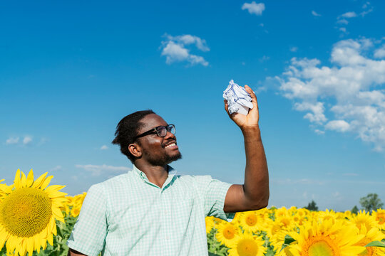 Smiling man looking at crumpled paper amidst sunflowers in field