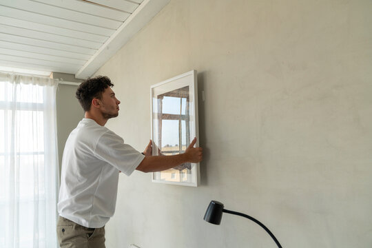 Young man hanging picture frame on wall at home