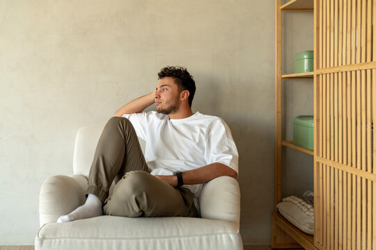 Young man sitting on armchair near wall at home
