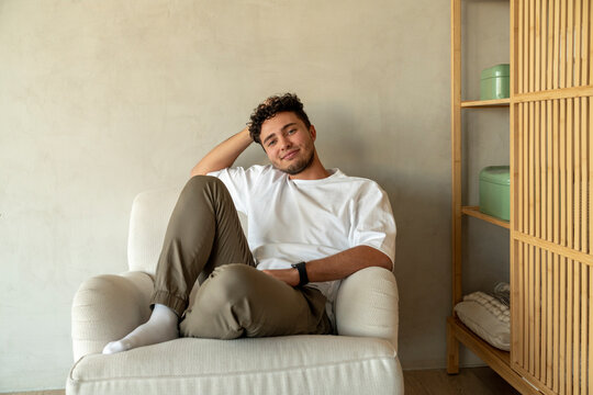 Smiling young man sitting on armchair at home