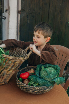 Smiling boy with vegetables in vintage wicker basket at table in backyard