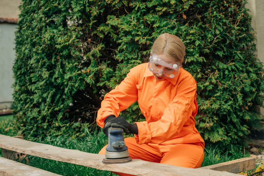 Woman in orange protective workwear polishing plank in backyard