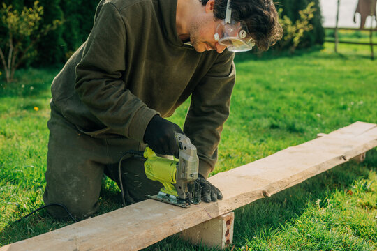 Man cutting plank with electric saw in backyard