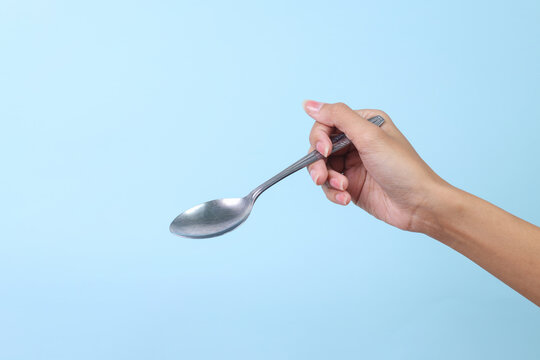 Woman's hand holds a stainless spoon on a blue pastel background.