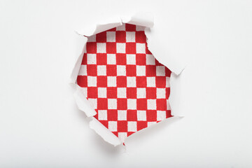 Torn hole in white paper revealing red and white checkered textile background. Restaurant tablecloth.