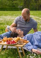Happy pregnant couple spends time together on a picnic, outdoors. A pregnant woman lies on her...