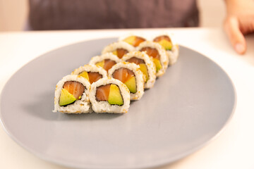 A plate of sushi with a person's hand in the background. The sushi is cut into pieces and arranged on a blue plate