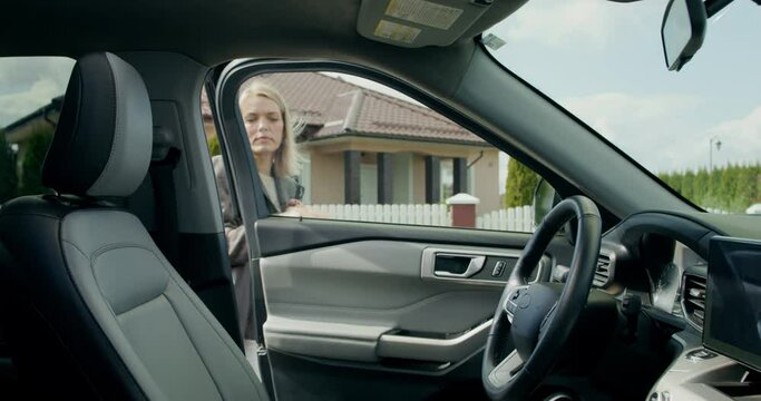 A blonde businesswoman gets into a car parked near the cottage and paints her lips looking in the mirro