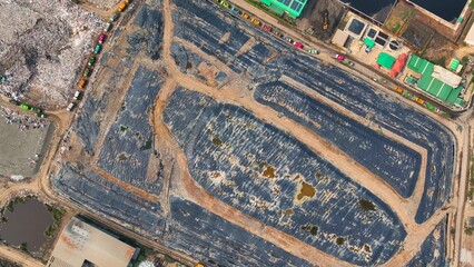 A bird's eye view uncovers a landfill veiled by layers of black plastic, futilely concealing our relentless consumption. Landfill background. Aerial view.
