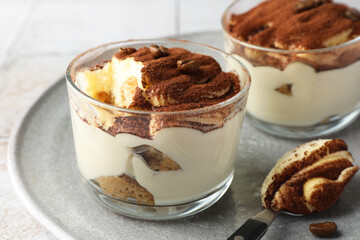 Delicious tiramisu in glasses, spoon and coffee beans on table, closeup