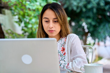 Young woman working on a laptop at a table outside on a patio at home