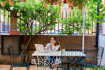 full view of a woman using her laptop computer in the patio of her house surrounded by plants