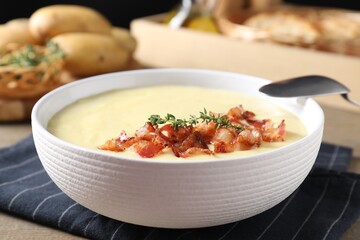 Tasty potato soup with bacon in bowl and spoon on table, closeup