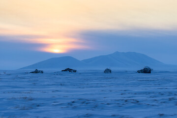 Abandoned houses in the tundra in the Arctic. Harsh polar climate. Winter arctic landscape. Evening view of the snow-covered tundra and snow-capped mountains. Cold winter weather. Northern nature.