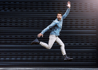 Man, jump and wave on dark background for energy, positive emotion and carefree in urban city. Young people, excited and cheerful body gesture for joy, happy and fun movement in air with mockup