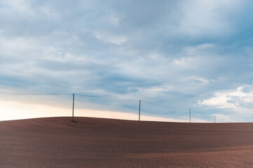 Spring minimalism with a row of electricity poles on clean cultivated agricultural field in Latvia