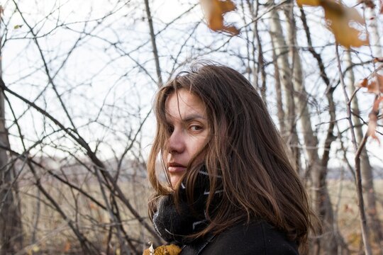 Young woman in sparse forest with worried expression, looking at camera