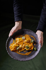 ravioli on a dark plate in hands, top view, vertical photo