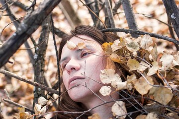 Thoughtful young woman lying on a bed of autumn leaves and branches - 791434596