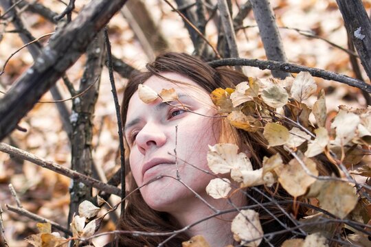 Thoughtful young woman lying on a bed of autumn leaves and branches