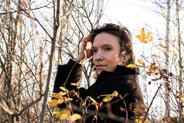 Fashionable woman in black coat by autumn trees, serene atmosphere.