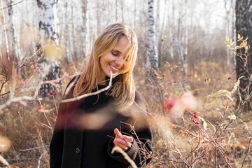 Happy woman in black coat collecting ripe berries in beautiful autumn woodland setting - 791435982