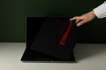 A graduate's hat on a laptop, on a green background.