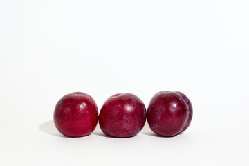 Three Fresh Red Plums Lined Up on a Bright White Background