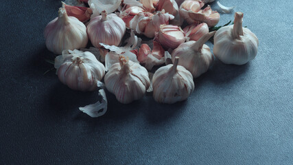 Whole and Split Garlic Bulbs on Dark Surface. Assortment of fresh garlic bulbs and cloves spread on a dark textured background.
