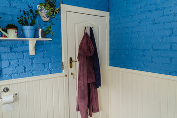 Isolated bathroom door with robes and pyjamas hanging on it and a shelf to the side