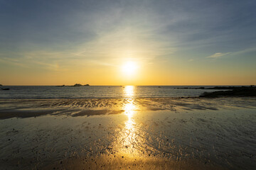 Fototapeta na wymiar Coucher de soleil teintant le ciel de nuances de bleu et de jaune, illuminant le sable mouillé de reflets dorés sur la côte du Finistère nord en Bretagne.